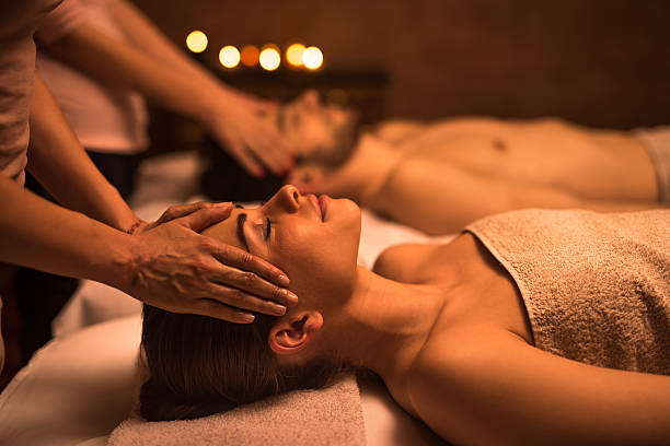 Couple relaxing at the spa during facial massage. Focus is on foreground, on young woman enjoying with eyes closed.